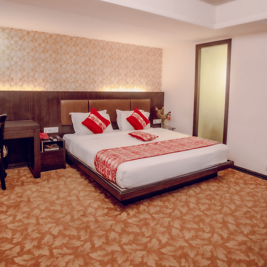 Executive room with king bed, red accents, wooden headboard with lighting, work desk, floral carpet, and warm decor at Viceroy Boutique Hotel, Kolkata.