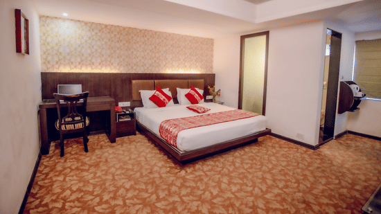 Executive room with king bed, red accents, wooden headboard with lighting, work desk, floral carpet, and warm decor at Viceroy Boutique Hotel, Kolkata.