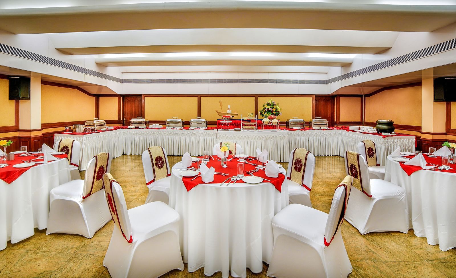 A banquet hall arranged for a formal dining event with red and white table settings and a tranquil ambiance. - Tara, Comfort Hotel in Hyderabad - Ramoji Film City.