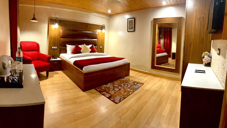 A spacious Deluxe Room with a bed, accent chair, and a TV at Mongas Hotel & Resort, Dalhousie.
