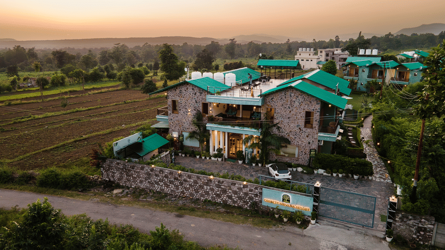 Aerial view of Corbett Nirvana Resort, Uttarakhand featuring cottage style two storey buildings and a farmland next to it.