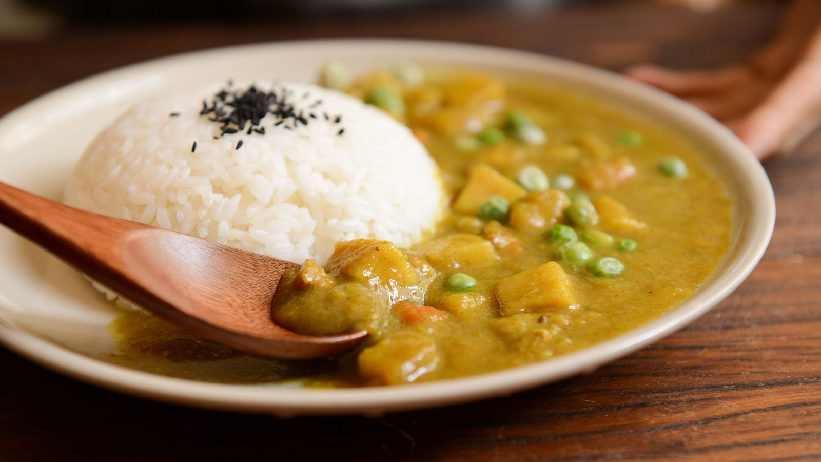 A bowl of curry with rice garnished with black sesame seeds on a wooden table
