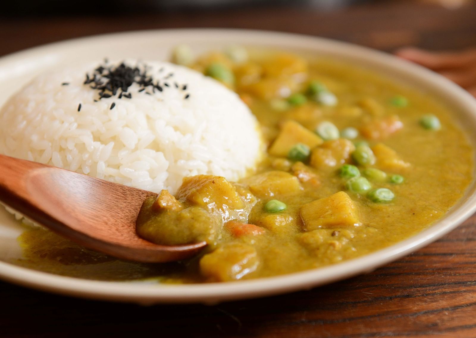 A bowl of curry with rice garnished with black sesame seeds on a wooden table