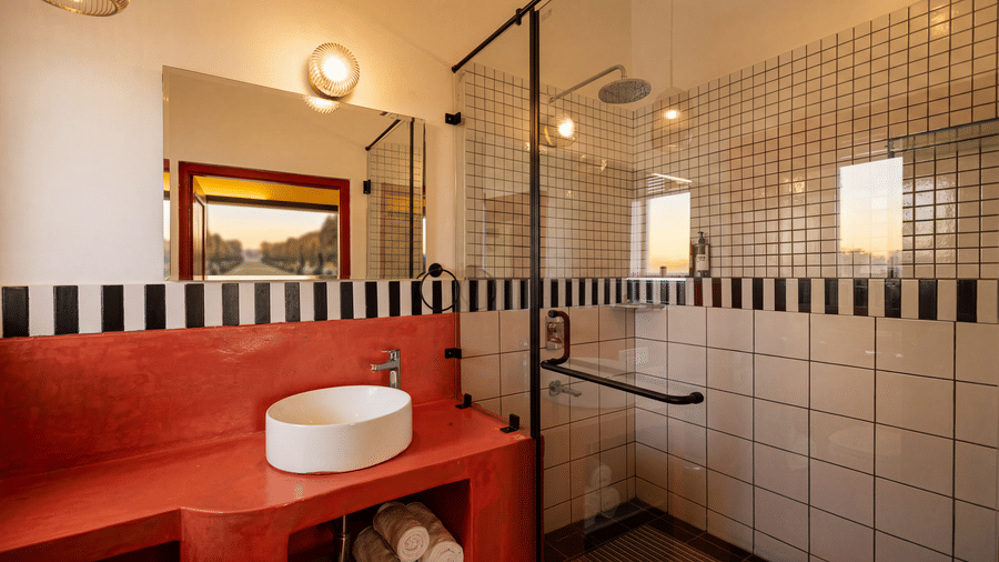 A washroom at The Sierra - By The Lake featuring an oval washbasin on a long vanity counter, a large mirror, and a glass enclosed shower cubicle.