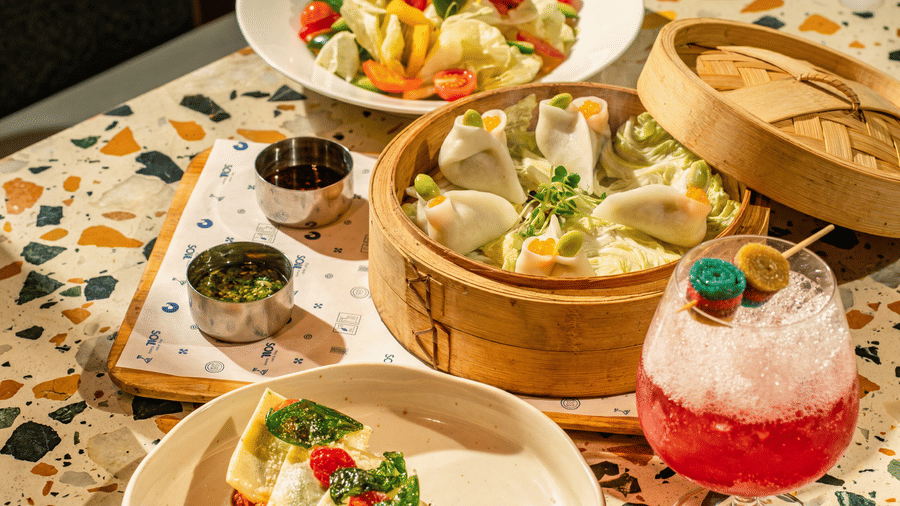 A spread of food bowls, sauces, dumplings in a basket, a drink served on a patterned table at The Sierra - By The Lake.
