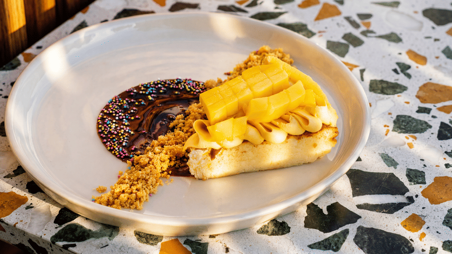 A slice of dessert cake topped with fruit slices is elegantly plated with syrup on a terrazzo tabletop at the property, The Sierra - By The Lake.