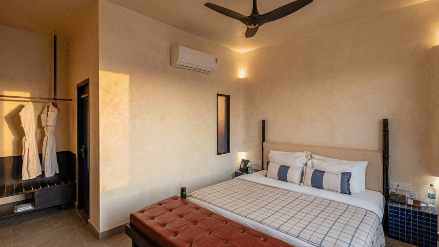 A cozy bedroom showcasing a double bed with pillows, ceiling fan, air conditioner, and hanging bathrobes at The Sierra - By The Lake.