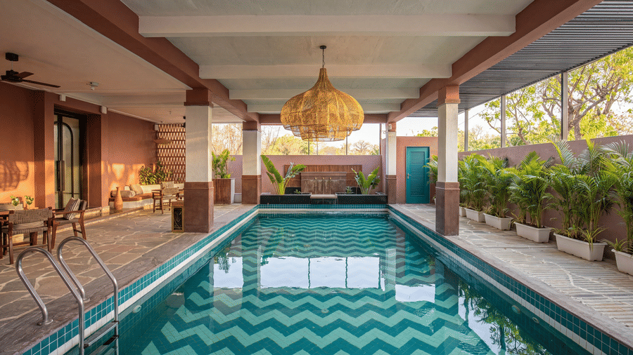 A symmetric view of a covered indoor swimming pool featuring hanging lamps, potted plants at The Sierra - By The Lake.