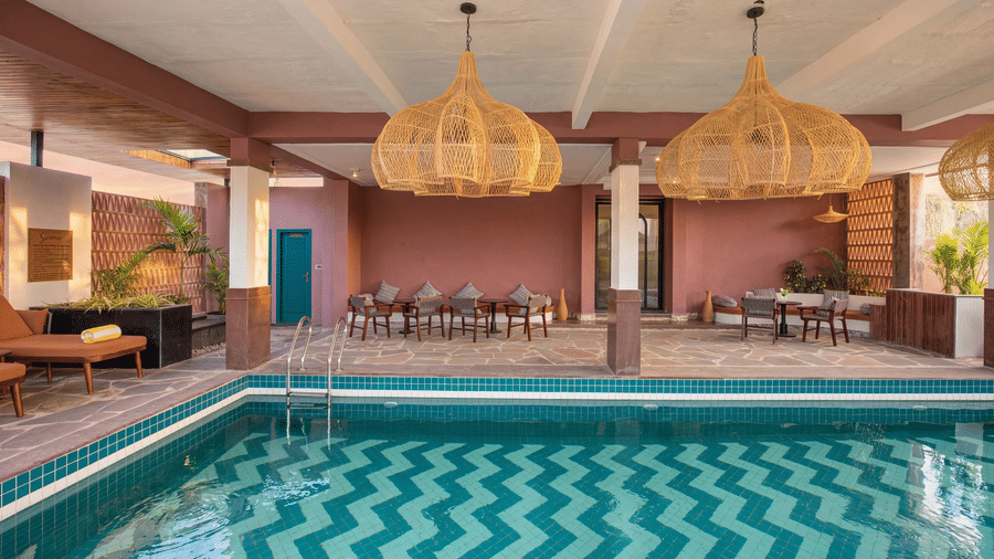 A swimming pool with a chevron tile pattern beneath large hanging lamps, dining tables at The Sierra - By The Lake.