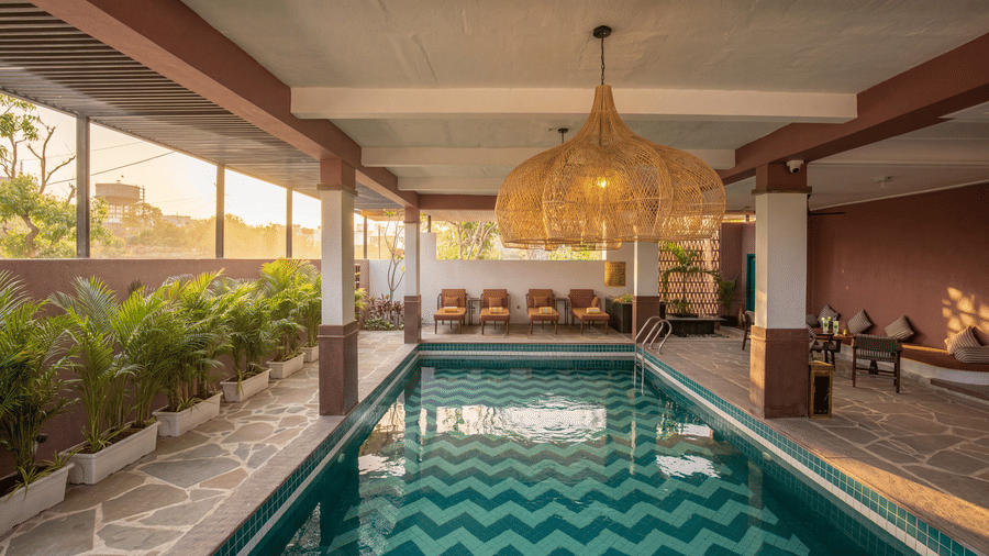 An indoor swimming pool flanked by a pathway of potted plants, columns, seating areas at The Sierra - By The Lake.