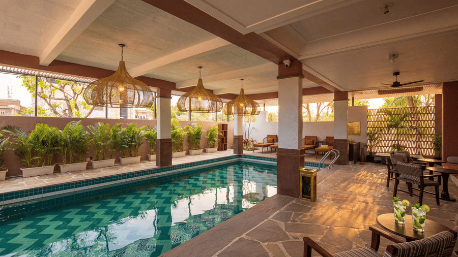 A wide view of an indoor swimming pool with poolside lounge tables, chairs, potted plants at The Sierra - By The Lake.