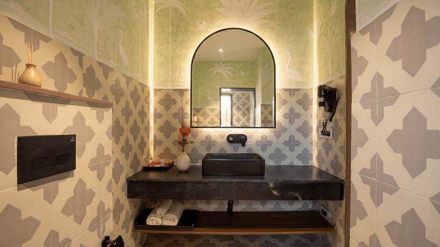 A washroom at The Sierra - By The Lake featuring a rectangular washbasin on a long vanity counter, an arched wall mirror, and patterned tiles.