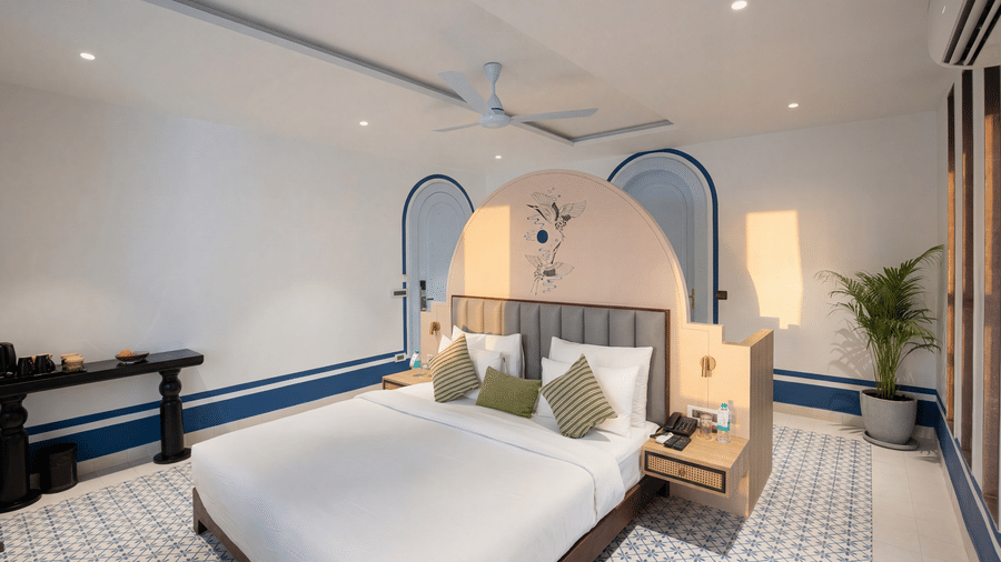 A bedroom at The Sierra - By The Lake featuring a king size bed with linen, a dark wooden side table, and double arched wall alcoves.