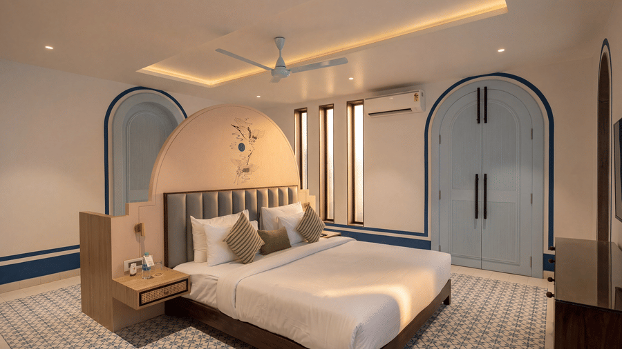 A bedroom at The Sierra - By The Lake featuring a king size bed with an upholstered headboard, a wooden bedside unit, and large arched doorways.