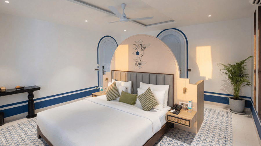 A bedroom at The Sierra - By The Lake featuring a king size bed with linen, a dark wooden side table, and double arched wall alcoves.