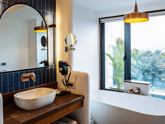 A bathroom featuring a standalone bathtub by a large window, a washbasin with an arched mirror, and a hanging light at The Sierra - By The Lake.