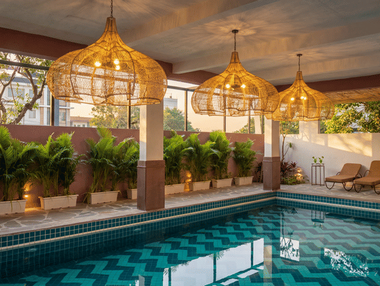 A swimming pool area illuminated by ornate hanging chandeliers next to a wall of hedges at The Sierra - By The Lake.