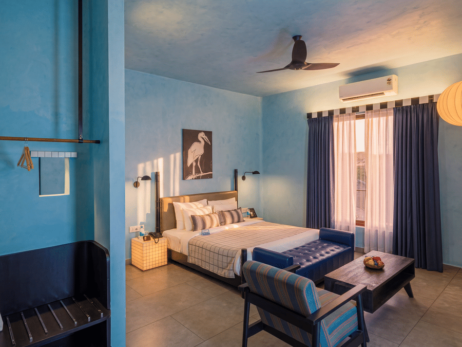 A modern bedroom with a king size bed, seating area, ceiling fan, large hanging lamp, and wardrobe at The Sierra - By The Lake.