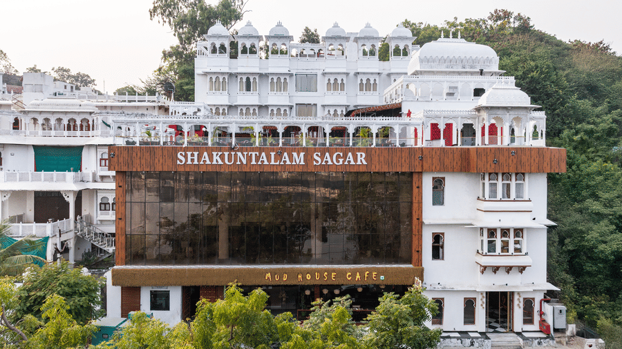 Daytime exterior shot of a multi-storey, white hotel complex nestled against a green hill.