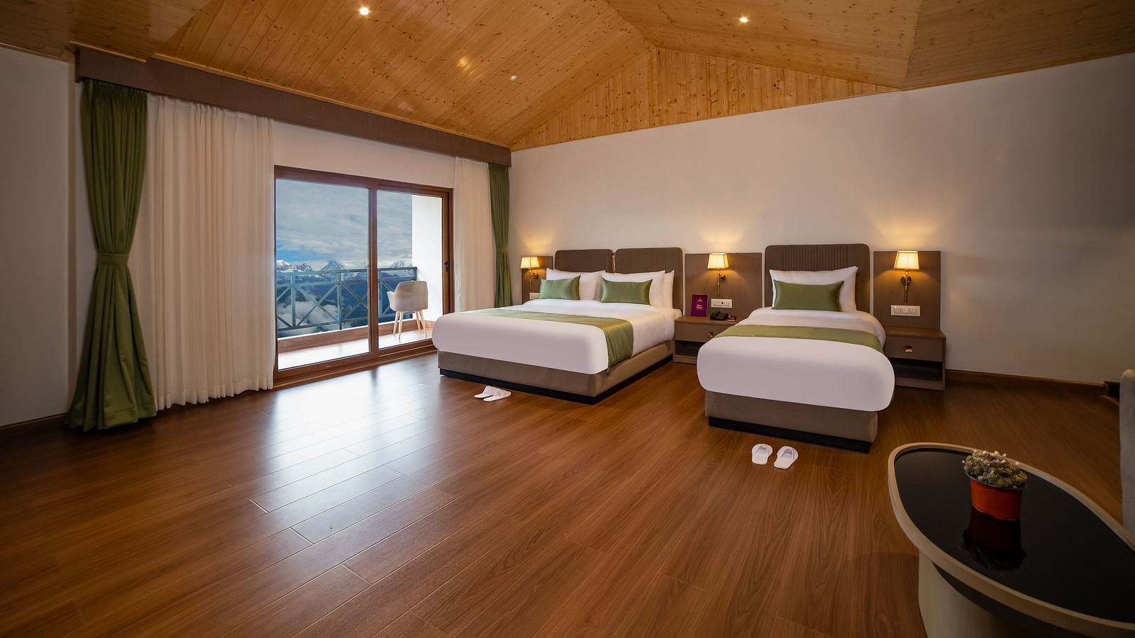 Spacious hotel room with two beds, wooden flooring, a large glass door leading to a balcony with mountain views, and cosy modern furnishings under a wooden ceiling - Yashshree Pelling Chekhim Retreat.
