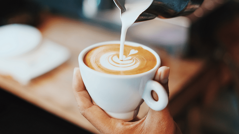 a person creating a pattern with milk foam on a cup of coffee