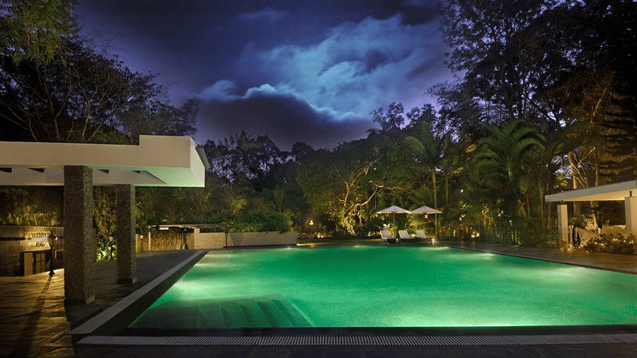 Outdoor swimming pool surrounded by trees during night with with dim light -Amanvana Spa Resort, Coorg - Luxury Resort
