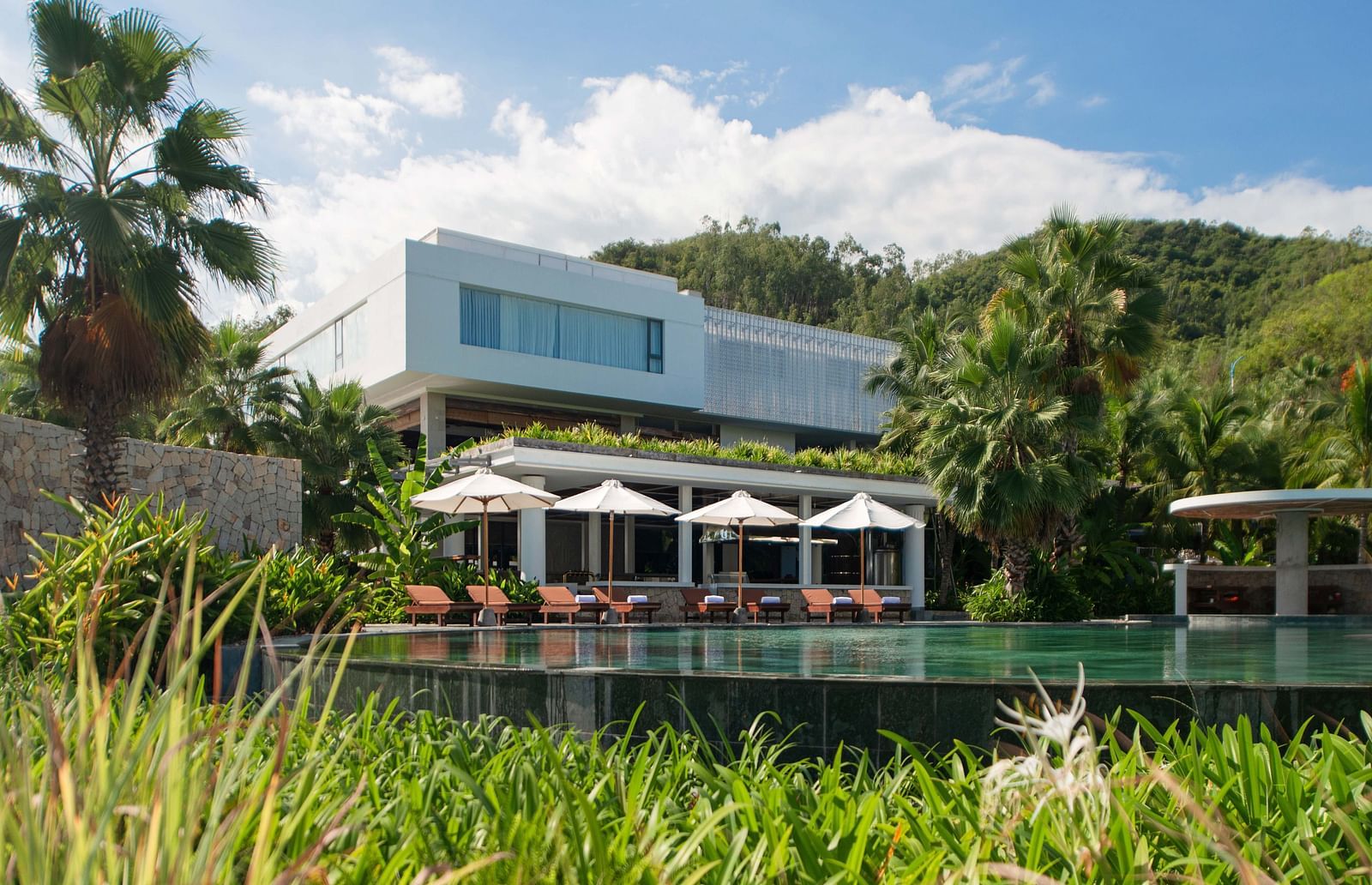 A garden side view of the resort with a well maintained pool in front during a sunny day - Alibu Resort Nha Trang
