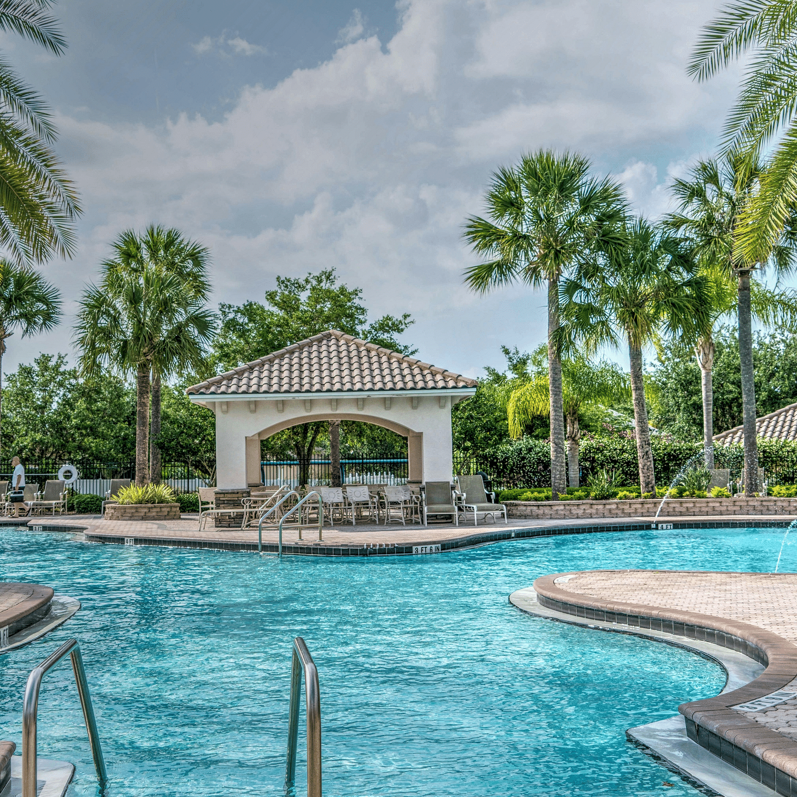 Swimming pool with palm trees at the side and a half cloudy sky