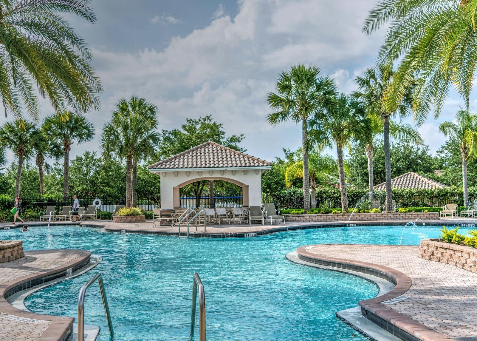 A serene outdoor swimming pool surrounded by palm trees and a cloudy sky