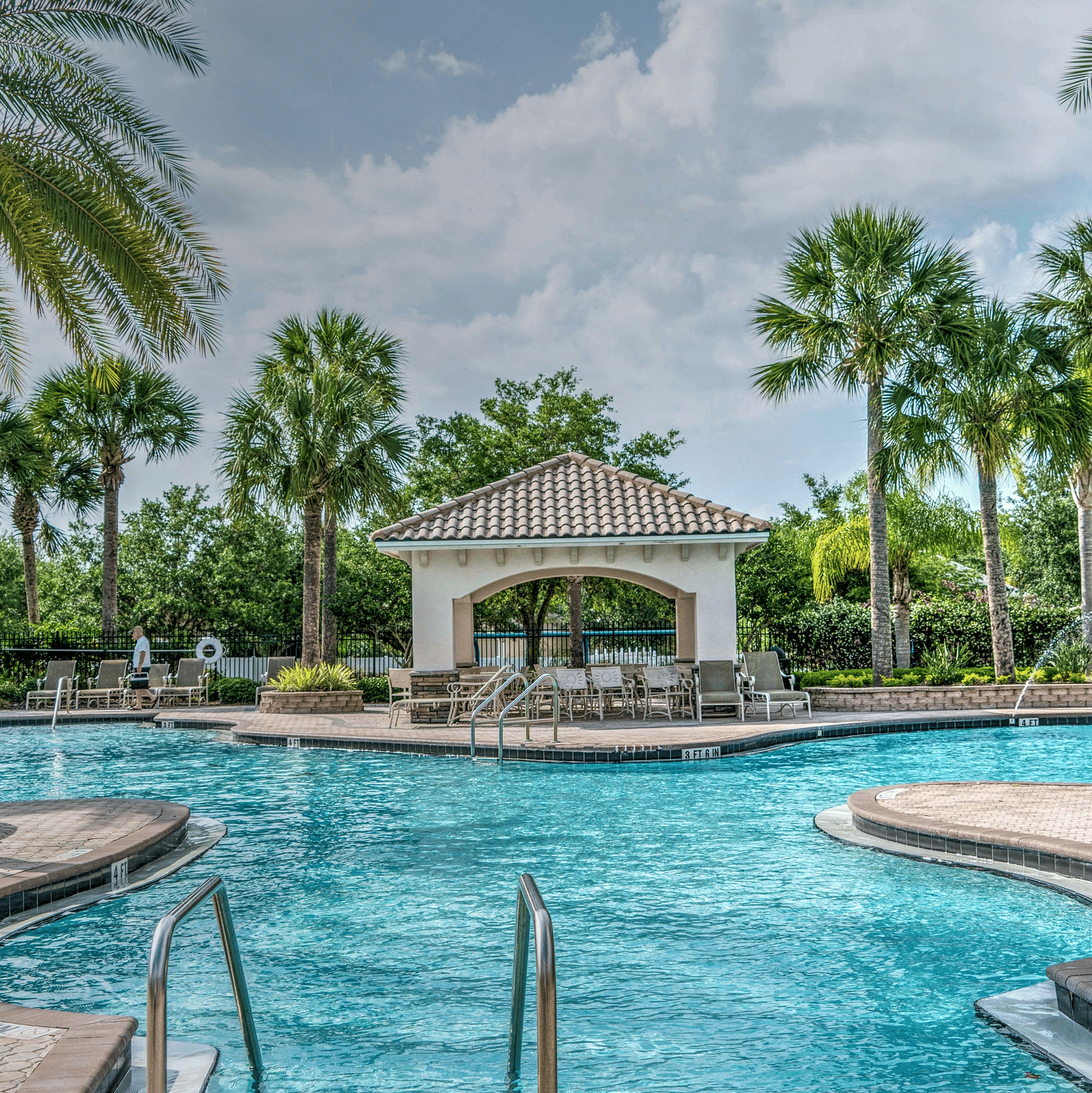 Swimming pool with palm trees at the side and a half cloudy sky