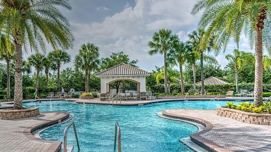 A view of the swimming pool surrounded by palm trees, set against a partly cloudy sky.