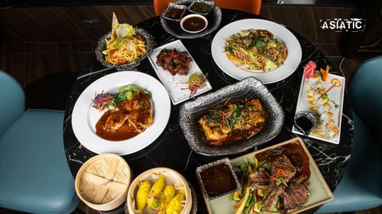 Table with assorted dishes, bowls, bread, and sides arranged for a meal at Asiatic Lounge.