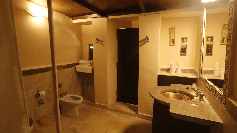 A bathroom with a glass-enclosed shower, washbasin with mirror, toilet, and tiled walls at Infinity Resorts Bandhavgarh.