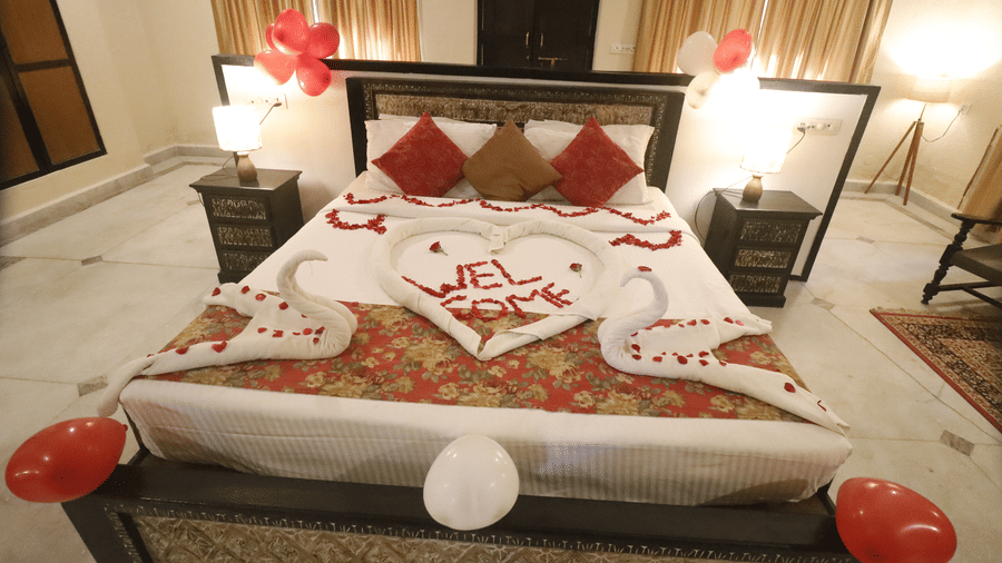A bedroom with a double bed decorated using flower arrangements and towel art, with side tables and lamps at Infinity Resorts Bandhavgarh.