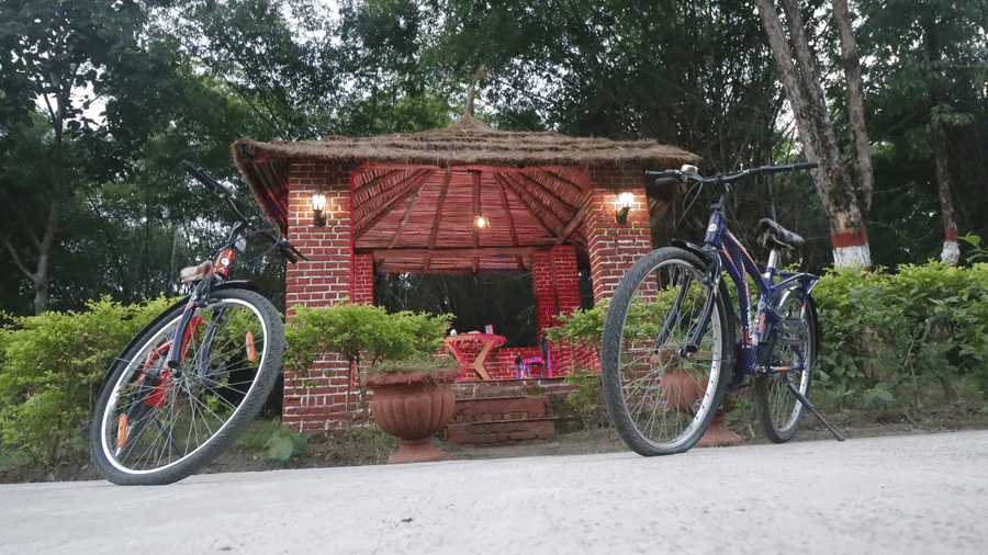 The entrance area with a small cottage structure and 2 bicycles parked in front, surrounded by trees at Infinity Resorts Bandhavgarh.
