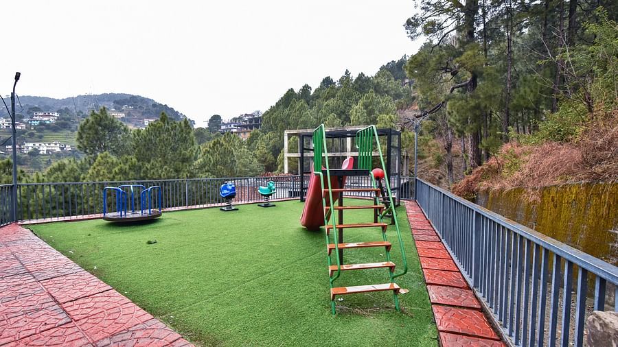 A children's play area with a slide and colourful play equipment on a well-maintained grassy surface, surrounded by a fence and beautiful views.