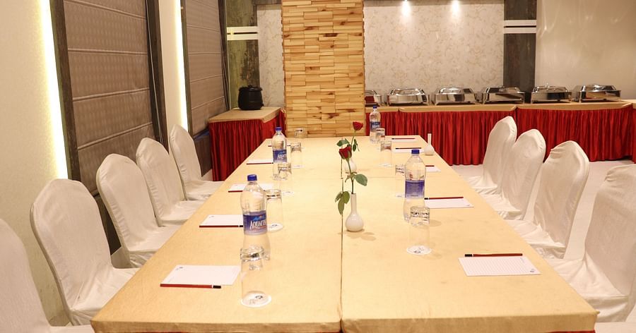 A front view of a large table with chairs on both sides, neatly arranged with stationery and water bottles at Hotel Uday Palace.