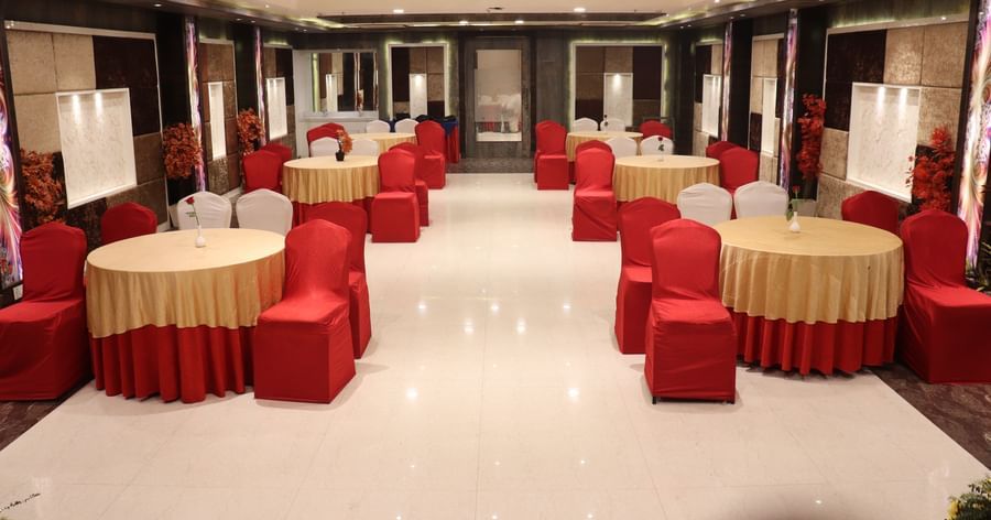 A spacious banquet hall with red and gold table settings for a group of people, and elegant interior design among the premier banquet halls in Varanasi - Hotel Uday Palace.