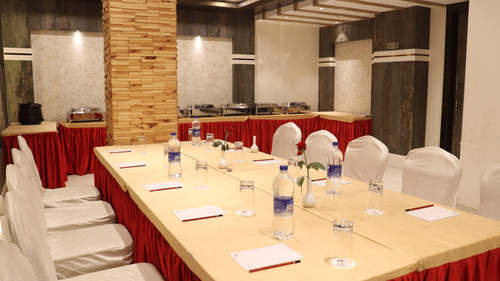A close-up view of a large table with chairs on both sides, set with stationery and water bottles at Hotel Uday Palace.