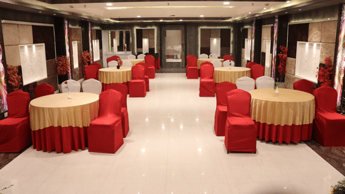 A spacious banquet hall in Varanasi with red and gold table settings for a group of people, and elegant interior design among the premier banquet halls in Varanasi - Hotel Uday Palace.
