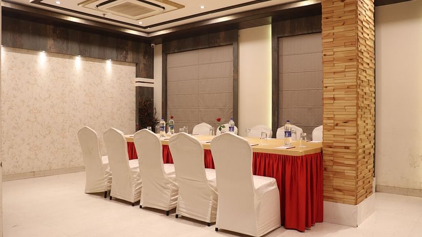 A large table with chairs on both sides, illuminated by bright lighting at Hotel Uday Palace.