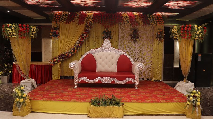A stage with a cushioned sofa, a well-decorated dais, and an elegantly designed background at Hotel Uday Palace.