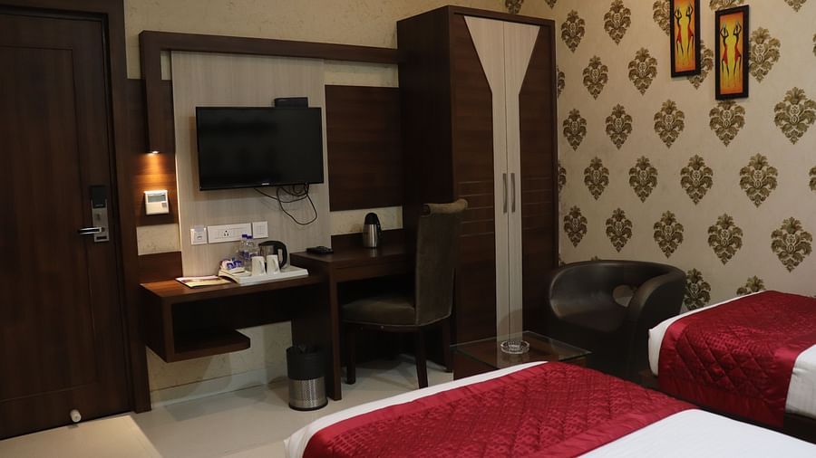 A spacious room showing the foot of the bed, a wall-mounted table below the TV, and a cupboard to the side at Hotel Uday Palace.