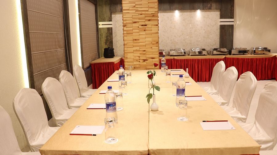 A front view of a large table with chairs on both sides, neatly arranged with stationery and water bottles at Hotel Uday Palace.