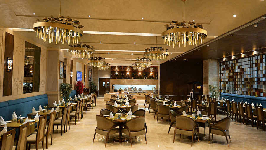 A spacious and elegantly decorated dining area at The Gaurs Sarovar Premiere, with multiple tables and chairs arranged for guests. Stylish lighting fixtures enhance the ambiance.