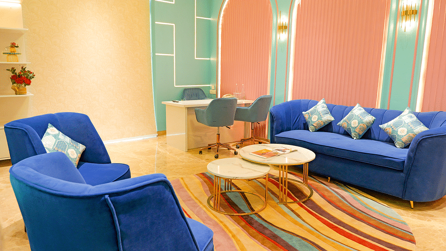 Top side view of the same lounge area at The Gaurs Sarovar Premiere, showing a different arrangement of the blue armchairs and the patterned rug