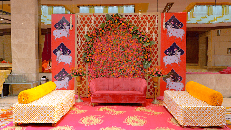 An elaborately decorated seating area at The Gaurs Sarovar Premiere, likely for a bride and groom at a wedding ceremony, with cushions and floral backdrops.