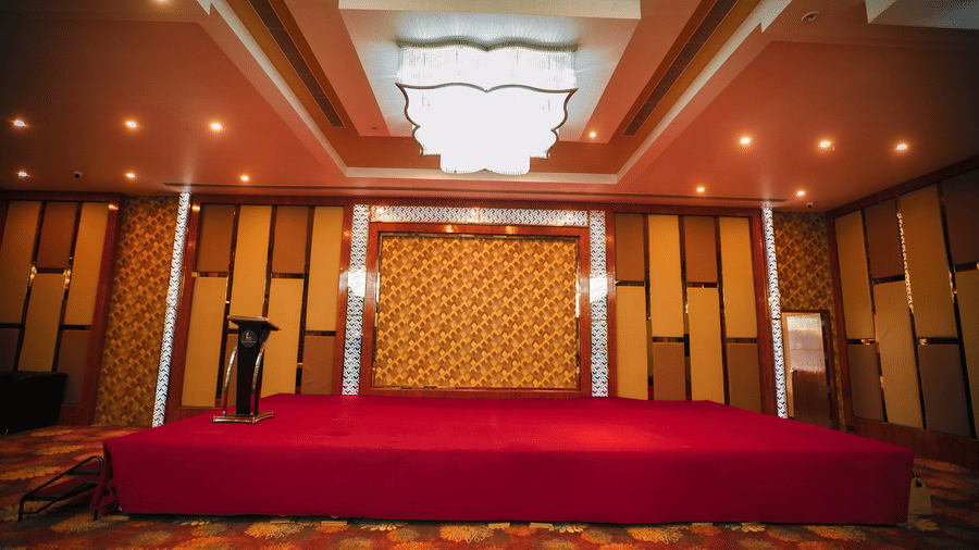 A professional indoor event stage featuring a red carpet, decorative wood paneling, and warm recessed lighting - Leroy Grand, Yeshwanthpur