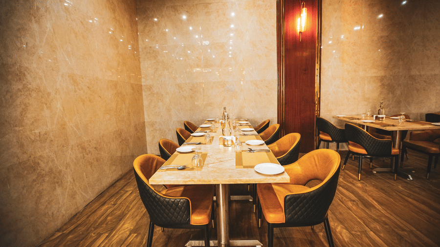 An intimate indoor dining space with a long wooden table, yellow upholstered chairs, and marble-textured walls - Leroy Grand, Yeshwanthpur