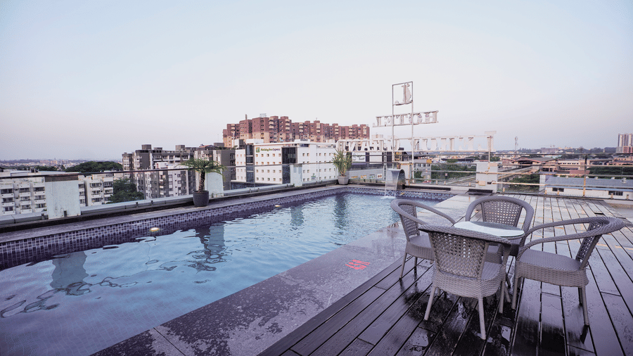 A stunning rooftop infinity pool with a wooden deck and patio seating overlooking the city skyline - Leroy Grand, Yeshwanthpur